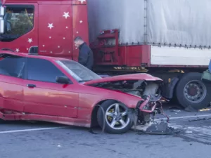 A Red Car With A Crushed Front End Sits In Front Of A Damaged Semi-Truck After A Serious Crash, Showing The Types Of Collisions An Arlington Truck Accident Lawyer Helps Clients Navigate.