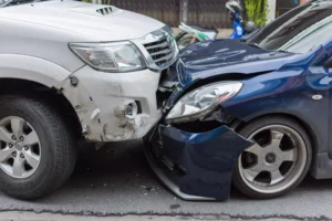 A Damaged Blue Sedan And A White Suv Collide Head-On In The Middle Of A Street, Emphasizing The Serious Nature Of These Crashes And The Importance Of Contacting A Dallas Head-On Collision Lawyer For Legal Guidance And Compensation.