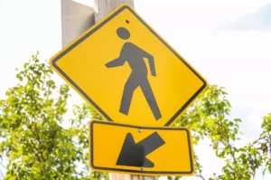 Yellow Pedestrian Crossing Sign With Directional Arrow Below, Often Seen In Areas With High Foot Traffic, Highlighting The Importance Of Awareness Around Common Causes Of Pedestrian Accidents.
