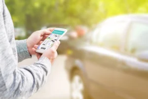 A Person Holds A Smartphone With The Lyft App Open While Standing Near A Parked Car, Representing The Growing Use Of Rideshare Services And The Need For A Dallas Lyft Accident Lawyer After An Injury Involving A Lyft Driver.