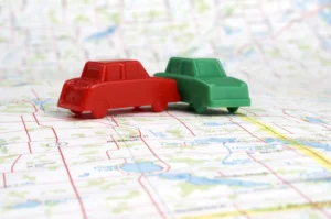 Two Toy Cars, One Red And One Green, Are Positioned In A T-Bone Collision On Top Of A Road Map, Symbolizing Intersection Crashes And The Importance Of Hiring An Experienced Dallas T-Bone Accident Lawyer To Navigate Injury Claims.