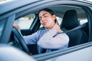 A Woman Sits In The Driver’s Seat Of Her Car, Wincing In Pain While Holding Her Neck After A Crash—An Injury Commonly Linked To Rear-End Collisions—Highlighting The Need For A Dallas Whiplash Car Accident Lawyer To Pursue Compensation.