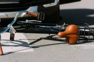 A Fallen Bicycle With A Damaged Tire Lying On The Road In Front Of A Car, Representing A Collision Scenario. Desoto Bike Accident Lawyer Can Help.