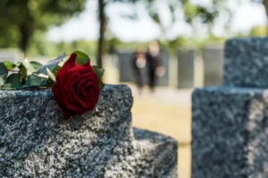 Red Rose Placed On A Gravestone With Blurred Mourners In The Background, Symbolizing Loss And The Need For A Desoto Wrongful Death Lawyer.