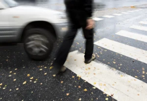 Blurry Image Of A Pedestrian Crossing A Street As A Car Approaches, Highlighting The Dangers Addressed By A Duncanville Pedestrian Accident Lawyer.