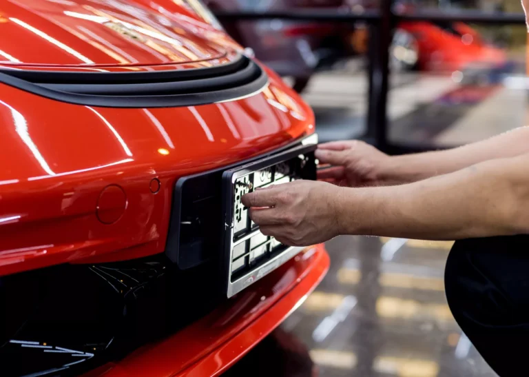 A person installing a front license plate on a red sports car in a garage. The image highlights the process of attaching a front license plate in Texas, which is required by state law for most vehicles.