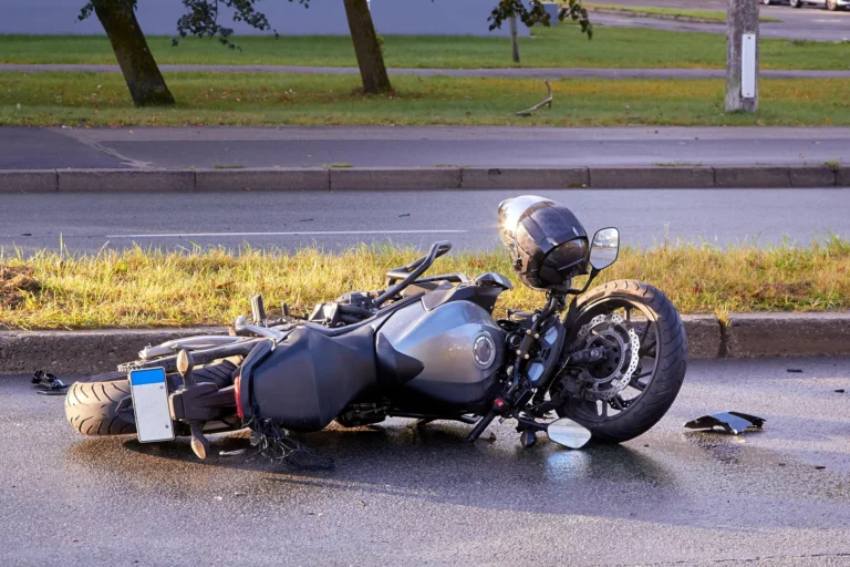 A Damaged Motorcycle Lying On Its Side On A Wet Road After An Accident, With A Helmet Still Attached To The Handlebars. This Image Illustrates What To Do After A Motorcycle Accident, Emphasizing The Importance Of Safety, Legal Steps, And Seeking Medical Attention.