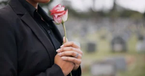 A Grieving Person In Black Holding A Rose At A Cemetery, Symbolizing Loss And Mourning, Representing The Emotional Impact Of Asking, &Quot;What Is A Wrongful Death Lawsuit?&Quot;