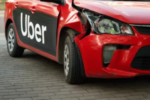 A Damaged Red Sedan With The Word “Uber” On The Side Is Parked On A Paved Surface, Symbolizing The Aftermath Of A Crash And The Need For An Experienced Dallas Uber Accident Lawyer To Help Victims Pursue Compensation.