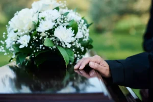 Hand Resting On A Casket Adorned With White Flowers, Representing The Grief And Loss Handled By A Wrongful Death Lawyer.